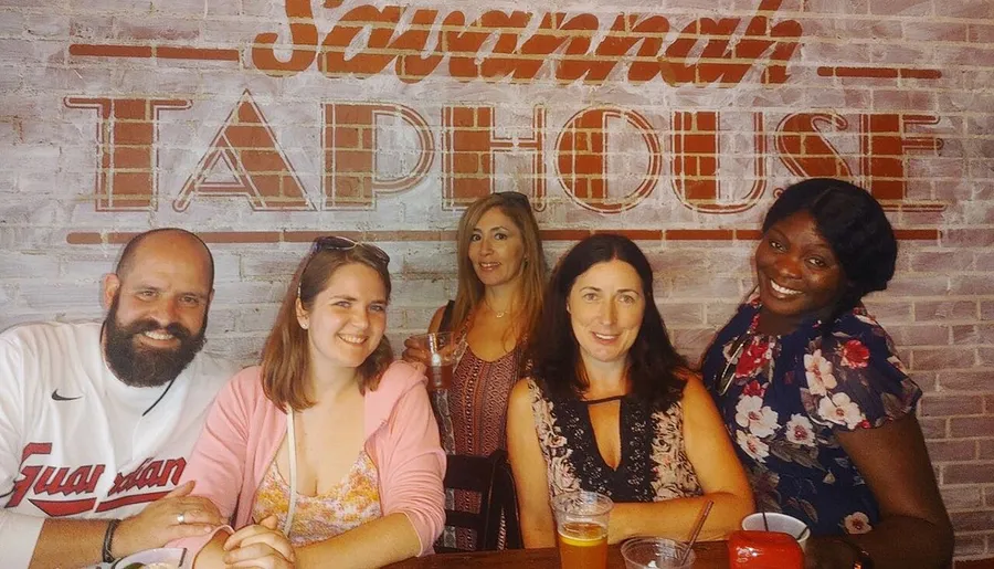 Five people are smiling for a photo at a table in front of a brick wall with the words Savannah Taphouse on it.