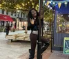 A person is playfully posed on a pole next to a mannequin dressed in a sparkling black outfit with outdoor dining and string lights in the background