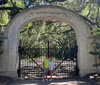 Two people are posing in front of an ornate gate with the inscription 1733 WORMSLOE 1913 surrounded by lush greenery and hanging Spanish moss