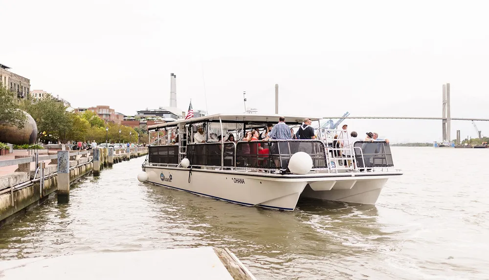 A group of people is enjoying a ride on a riverboat named Ohana that is docked along a city waterfront