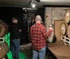 A person in a red plaid shirt is taking a photo in a room with whiskey barrels and a few other individuals