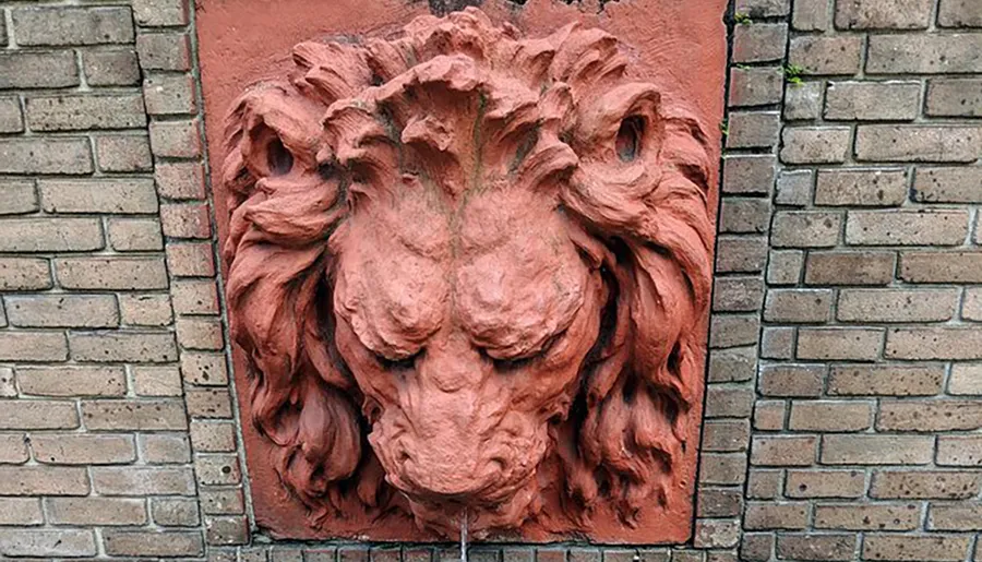 The image shows a terracotta relief sculpture of a lion's head set into a brick wall.