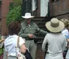 A person wearing a wide-brimmed hat and a uniform is speaking to a group of attentive women on a city street