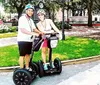 Two people smiling and standing with their Segways in a sunny park setting