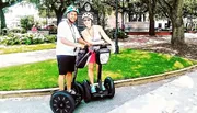 Two people smiling and standing with their Segways in a sunny park setting.