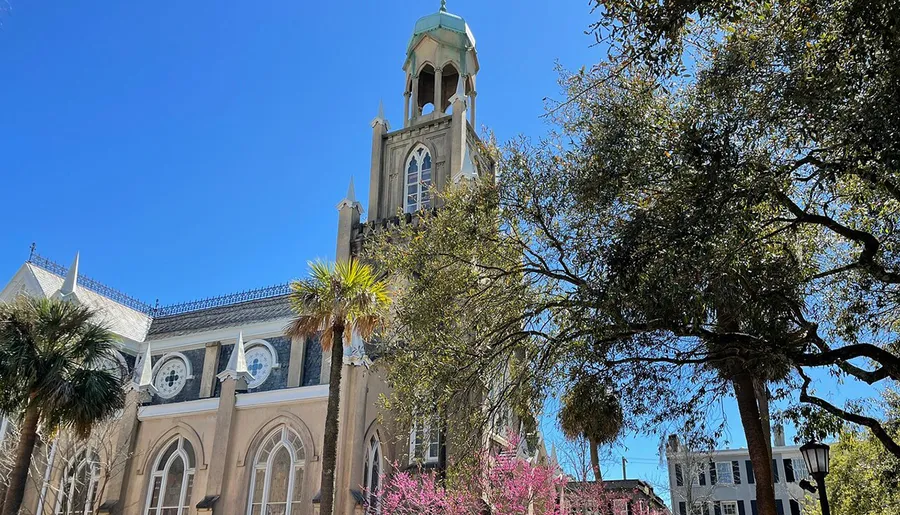 The image shows a picturesque view of a historic church with a distinctive green dome and spire, framed by lush trees against a clear blue sky.