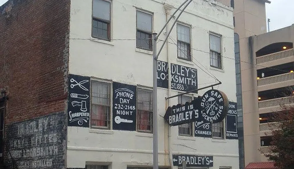 The image shows the exterior of a building with various vintage signage advertising a locksmith business including different services such as keys cut locks changed and sharpening with a clear contrast between the historic building and the modern parking structure adjacent to it