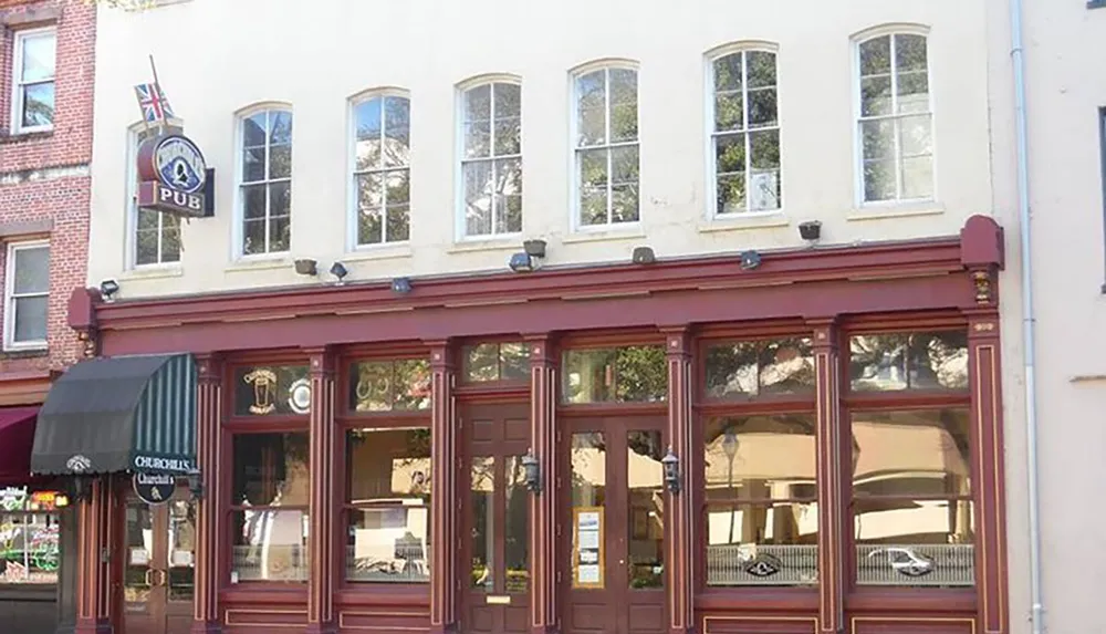 The image shows the facade of a quaint traditional pub with a British flag-themed sign large windows and a dark red storefront