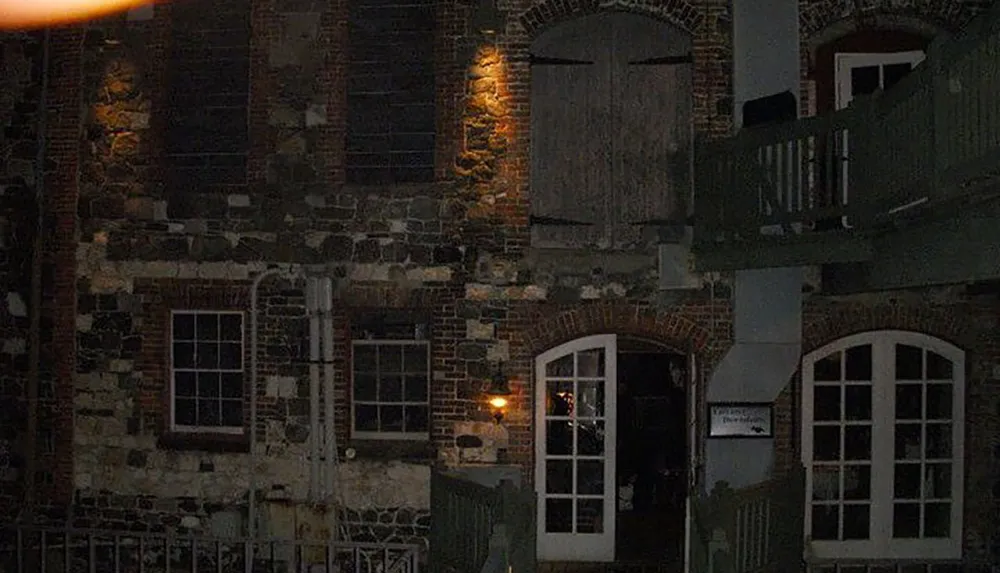 This is a dimly lit nocturnal image of an old brick building with windows some with shutters an open door and a balcony creating a slightly eerie atmosphere