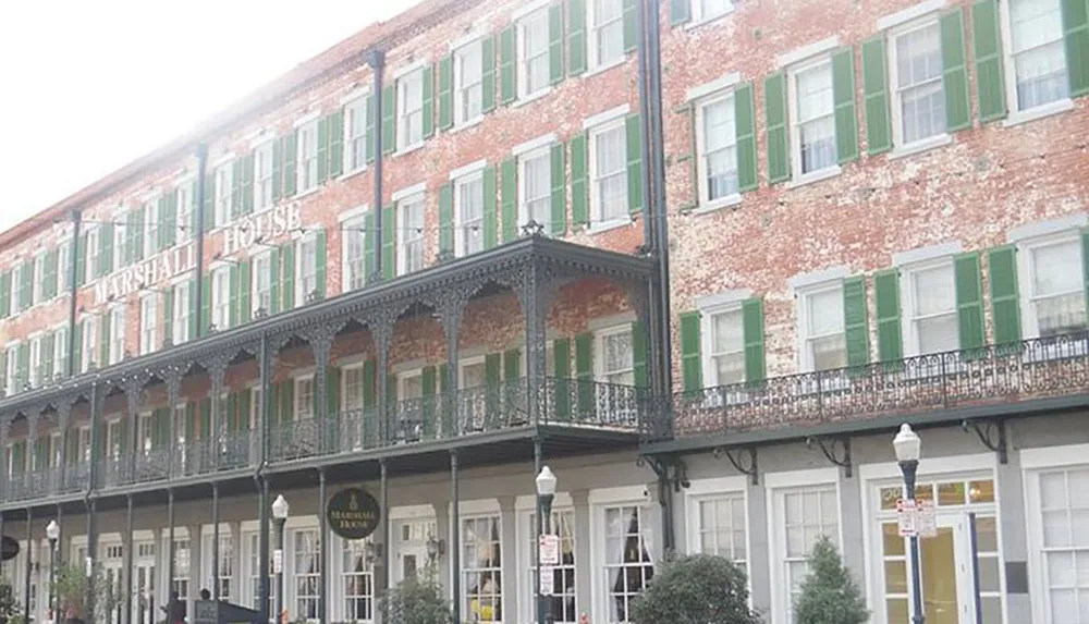 The image shows the exterior of the historic Marshall House featuring its distinctive red brick facade with green shutters and ornate black wrought iron balconies