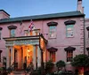 This image shows the facade of The Olde Pink House an elegant pink-colored historical building housing a restaurant and tavern flying both the American and British flags at dusk