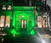 The image depicts a building entrance illuminated with green lights at night giving it an eerie and dramatic appearance