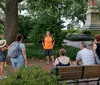 A group of people is attentively listening to a tour guide who is standing in front of them in an urban park setting