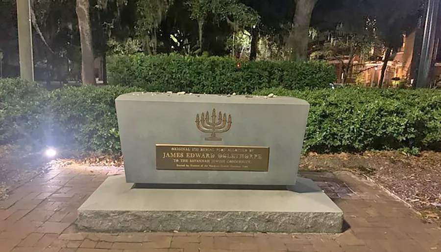 The image shows a stone monument with a menorah and a plaque dedicated to James Edward Oglethorpe, acknowledging his historical significance to the Savannah Jewish community.