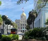 The image captures a sunlit street view with lush green trees a trolley bus and buildings leading up to a prominent structure with a golden dome and an American flag flying atop