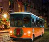 An orange vintage-style trolley adorned with a Christmas wreath travels down a festive cobblestone street at night