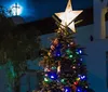 An orange vintage-style trolley adorned with a Christmas wreath travels down a festive cobblestone street at night