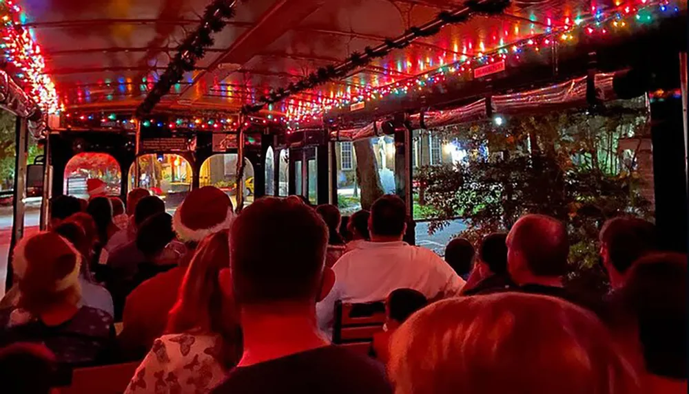 Passengers are enjoying a festive night ride on a trolley bus adorned with colorful Christmas lights