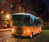 A brightly lit orange trolley with holiday decorations is driving down a festive street at night