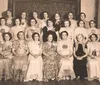 The image shows a group of women in formal attire posing for a black-and-white photograph likely from an early to mid-20th-century setting