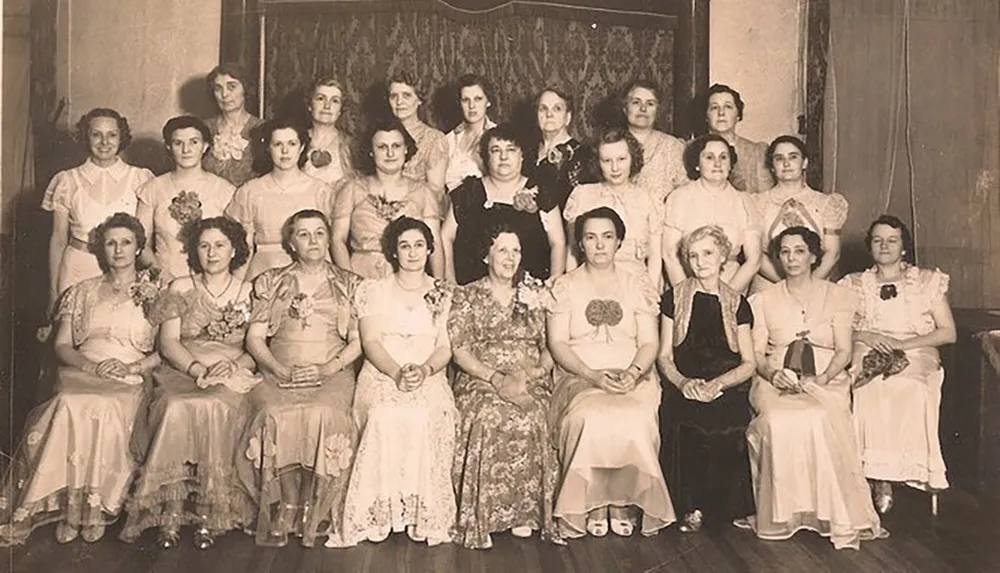 The image shows a group of women in formal attire posing for a black-and-white photograph likely from an early to mid-20th-century setting