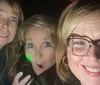Three women are taking a close-up selfie in a dimly lit environment displaying a range of expressions from surprise to smiles