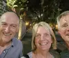Three smiling people are taking a selfie together at night on a tree-lined path