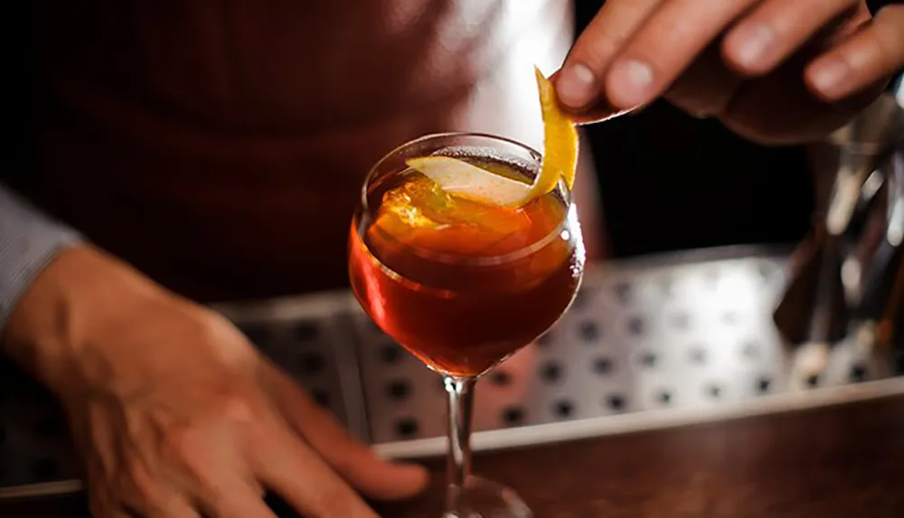 A bartender is garnishing a cocktail with a citrus peel