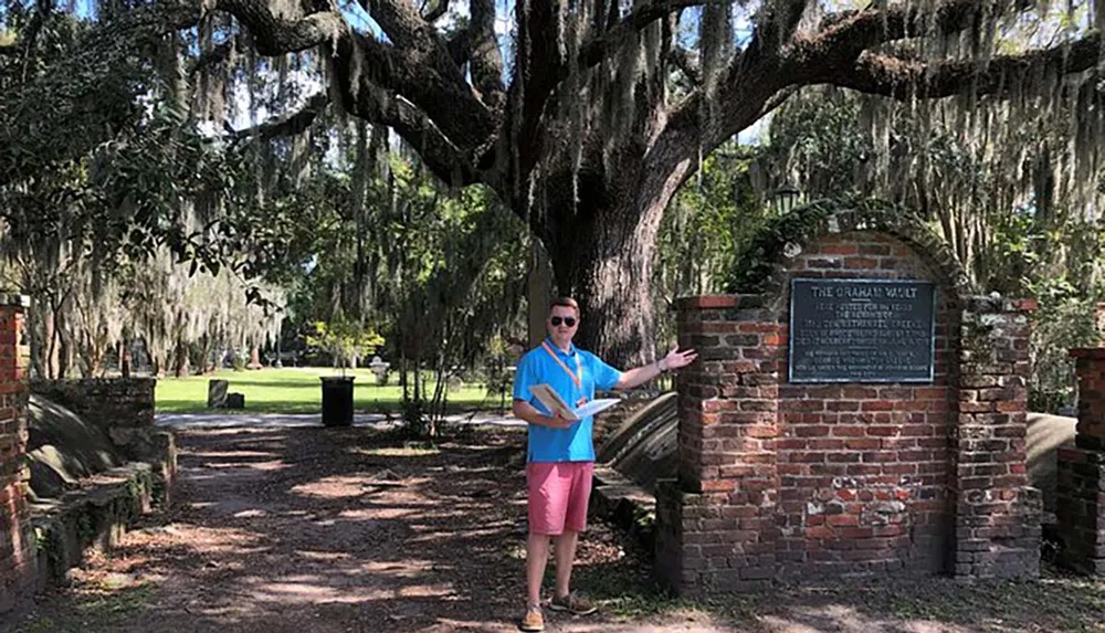 A person is standing by a historic marker called The Graham Vault under a large tree draped with Spanish moss