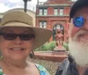 A smiling couple takes a selfie with a historic building possibly identified as the Savannah Cotton Exchange and a lion statue in the background