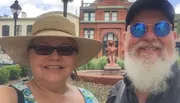A smiling couple takes a selfie with a historic building, possibly identified as the 