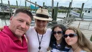 Four smiling individuals take a selfie on a sunny day at a boat dock.