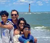 A family of four is smiling for a photo on a sunny day at the beach with a lighthouse visible in the background