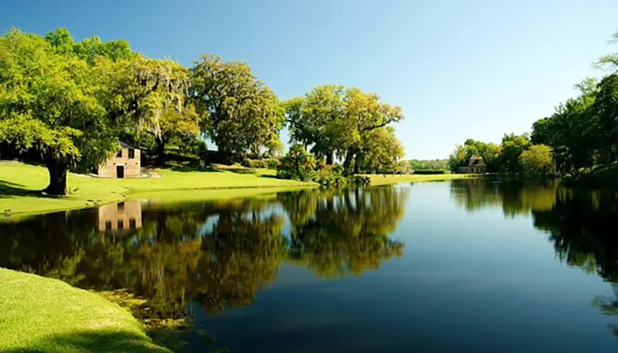 A serene landscape showcasing a calm lake reflecting the lush greenery and trees, with quaint buildings nestled among the foliage.