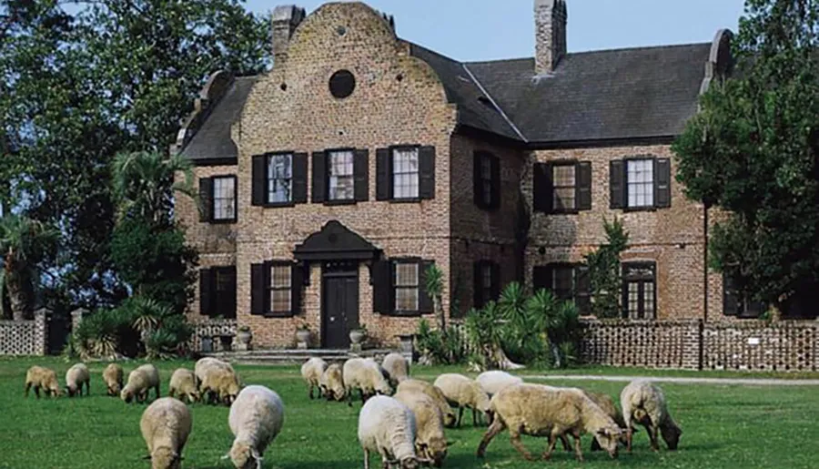 A flock of sheep grazes on the lawn in front of a quaint brick house with an asymmetrical façade and a distinctive stepped gable.