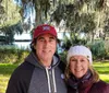 Two people are posing for a photo outdoors on a sunny day with Spanish moss hanging from the trees in the background suggesting a Southern US setting