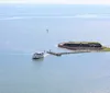 The image shows an aerial view of a coastal star-shaped fortress with a large flagpole at the forefront surrounded by water on three sides