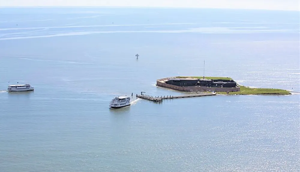 Two boats are approaching a small island with a jetty and a low-lying structure surrounded by a vast expanse of shimmering blue water