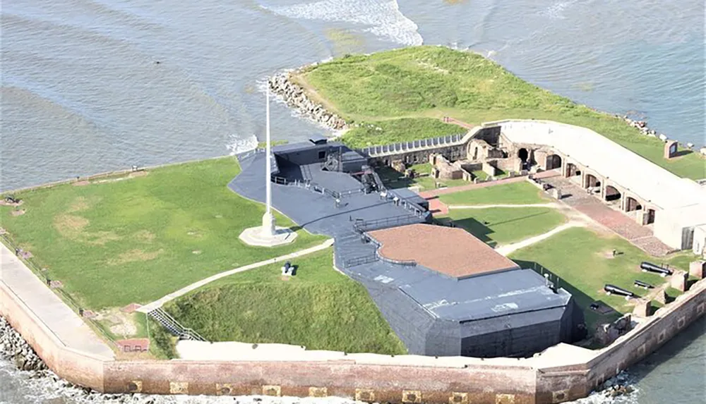 The image shows an aerial view of a coastal star-shaped fortress with a large flagpole at the forefront surrounded by water on three sides