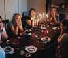 A group of surprised people sits at a dimly lit dinner table with lit candles appearing to react to an unexpected event