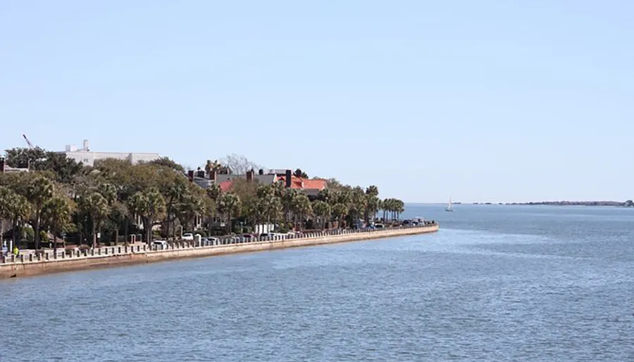 The image shows a waterfront promenade lined with palm trees and benches, with historical buildings in the background, under a clear blue sky.