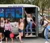 A group of cheerful people is posing with varied expressions and gestures in front of a shuttle bus that advertises local craft beer tours