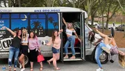 A group of cheerful people is posing with varied expressions and gestures in front of a shuttle bus that advertises local craft beer tours.