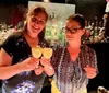 Two people are smiling and making drinks behind a bar with a variety of bottles in the background