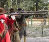 Three individuals dressed in historical attire are aiming long rifles in an outdoor setting that appears to simulate a scene from the past