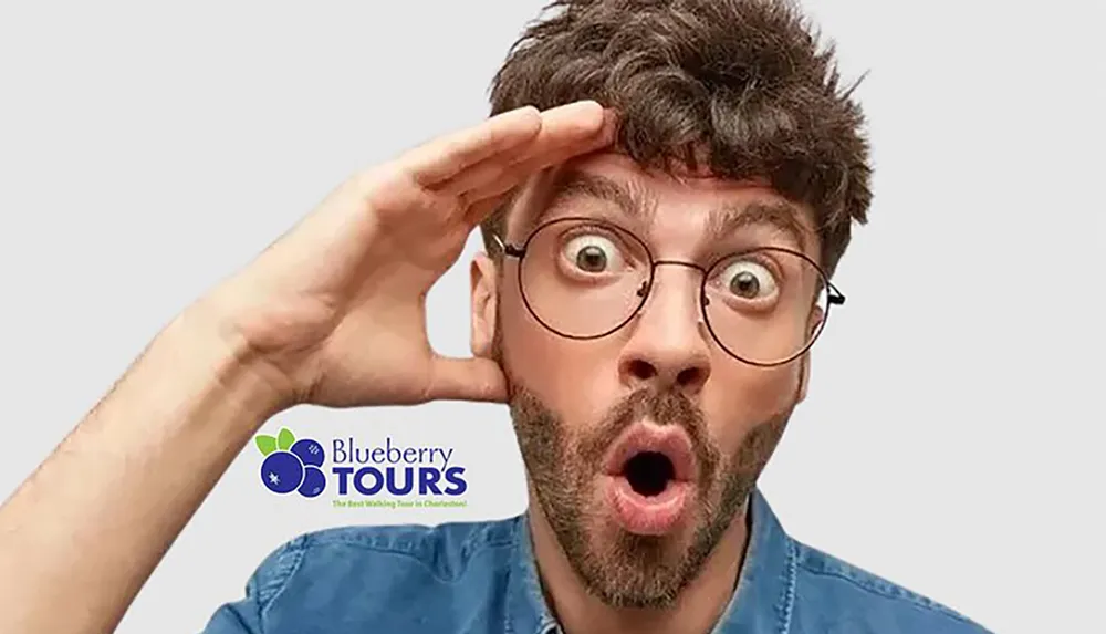 A man with round glasses is saluting with a surprised expression against a plain background with an overlaid logo for Blueberry Tours