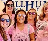 A group of five women wearing pink t-shirts and sunglasses are smiling in front of a sign that says WELLHUNG presumably at a vineyard or winery