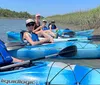 A group of smiling people are enjoying kayaking together on a sunny day in a calm waterway with grassy banks