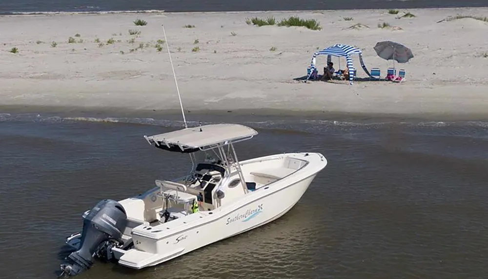 A boat is anchored near a sandy shore where people have set up a canopy and beach chairs