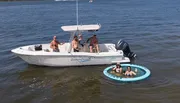 A group of people is enjoying a sunny day out on the water with some on a boat and others in an attached floating ring.